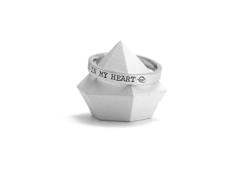 Op de afbeelding: Een zilveren ring met de inscriptie "You are in my heart" op een witte displaystandaard.