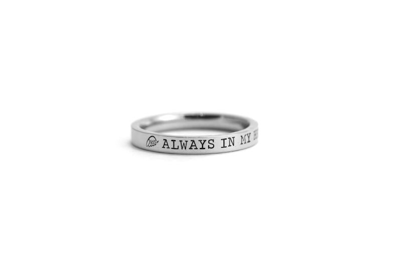 Op de afbeelding: Een zilveren ring met de inscriptie "ALWAYS IN MY HEART" en een klein vleugelontwerp.