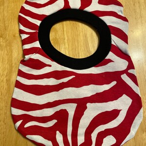 May include: Red and white zebra patterned fabric neck gaiter with a black fabric opening for the face.