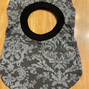 May include: A grey and white patterned fabric bib with a black trim around the neck opening.