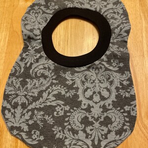 May include: A grey and white patterned fabric bib with a black elastic neckline.