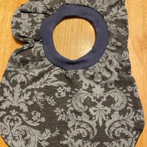 May include: A grey and white patterned fabric baby bib with a blue trim around the neck opening.