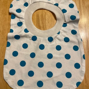 May include: White cotton bib with a teal polka dot pattern and a white ribbed neck opening.