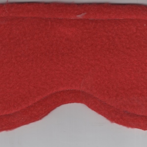 May include: Red sleep mask made of soft fleece fabric. The mask has a black elastic band for a comfortable fit.