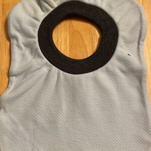 May include: A light blue baby bib with a dark grey trim around the neck opening. The bib has a textured surface.
