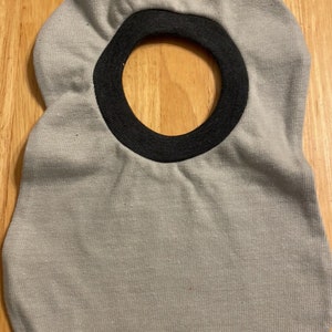 May include: A grey and black baby bib with a ruffled edge. The bib has a black trim around the neck opening.