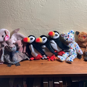 A collection of vintage Beanie Babies: a trio of bats, a trio of puffins, a confetti-ed white bear, an AyeAye, a cockatoo, and a penguin