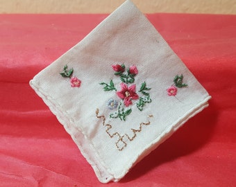 May include: White handkerchief with embroidered pink and red flowers, green leaves, and small blue flowers. The handkerchief has a scalloped edge and a stitched design in the corner.