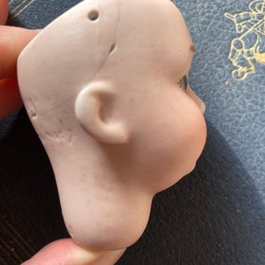 May include: A porcelain doll head with painted blue eyes and a crack on the side. The head is missing the body and has a hole on the top.