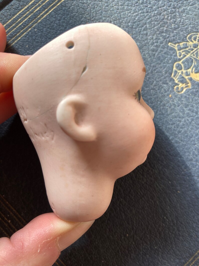 May include: A porcelain doll head with painted blue eyes and a crack on the side. The head is missing the body and has a hole on the top.