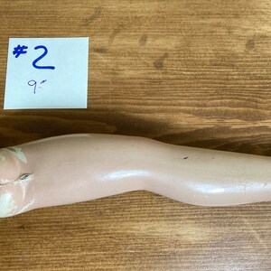 May include: A light pink, plaster doll leg with a metal hook at the top. The leg is 9 inches long. #2