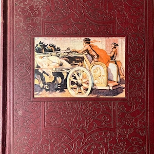 May include: A red book with a gold embossed design on the cover. The cover features a scene of a chariot pulled by horses with two people riding in it.