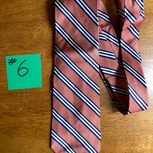 Puede incluir: Una corbata a rayas con fondo rojo y rayas blancas y azul marino. La corbata est&aacute; anudada y el nudo est&aacute; en el lado derecho de la imagen. La corbata est&aacute; sobre una superficie de madera. #6