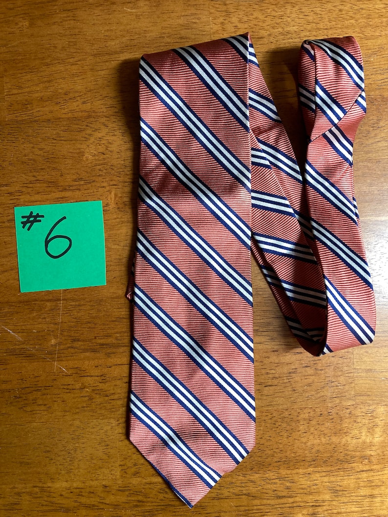 Puede incluir: Una corbata a rayas con fondo rojo y rayas blancas y azul marino. La corbata est&aacute; anudada y el nudo est&aacute; en el lado derecho de la imagen. La corbata est&aacute; sobre una superficie de madera. #6
