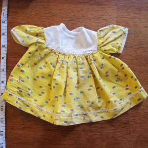 May include: A yellow dress with a white bodice and a small bow print. The dress has a white lace trim around the bottom.