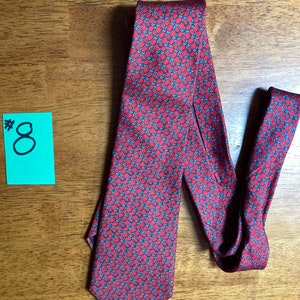 Puede incluir: Una corbata de seda roja con un patr&oacute;n geom&eacute;trico azul y blanco. La corbata tiene una punta puntiaguda y est&aacute; anudada.