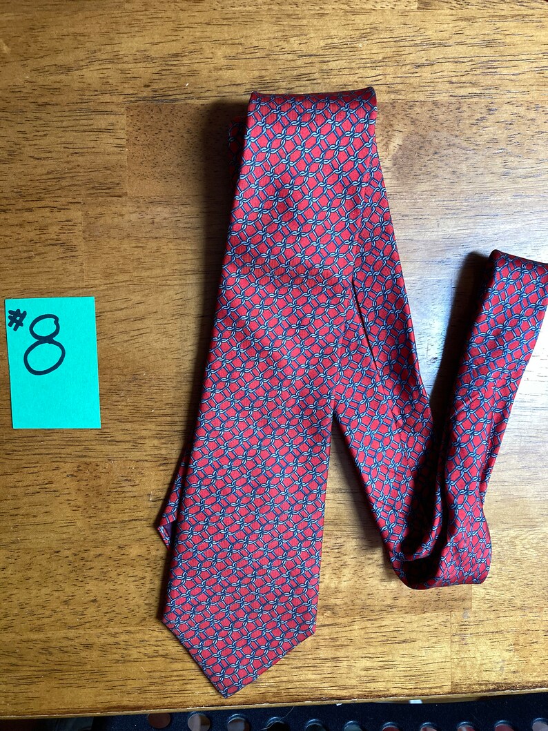 Puede incluir: Una corbata de seda roja con un patr&oacute;n geom&eacute;trico azul y blanco. La corbata tiene una punta puntiaguda y est&aacute; anudada.
