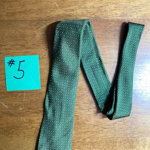 Puede incluir: Una corbata verde con un patr&oacute;n geom&eacute;trico blanco y negro. La corbata est&aacute; doblada en forma de N y tiene una etiqueta #5 en el lado izquierdo de la imagen.