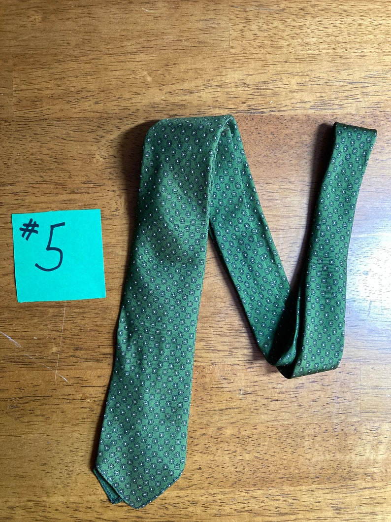 Puede incluir: Una corbata verde con un patr&oacute;n geom&eacute;trico blanco y negro. La corbata est&aacute; doblada en forma de N y tiene una etiqueta #5 en el lado izquierdo de la imagen.