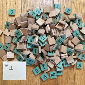 May include: A collection of wooden letter tiles with green letters, scattered on a wooden surface. The letters are in various fonts and sizes. A small white card with the number "1" is also present.