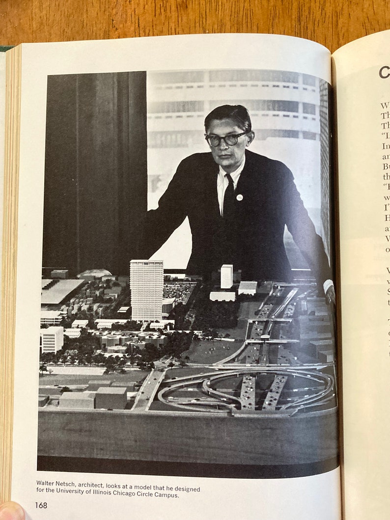 Puede incluir: Una foto en blanco y negro de un arquitecto mirando una maqueta de una ciudad. La maqueta incluye edificios, carreteras y una gran carretera circular.