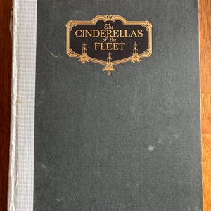 May include: A dark green book cover with gold lettering that reads "The Cinderellas of the Fleet".