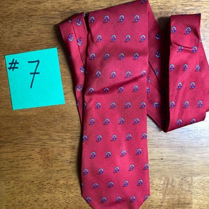 Puede incluir: Una corbata de seda roja con un patr&oacute;n repetido de c&iacute;rculos azules y blancos. La corbata tiene una punta puntiaguda.