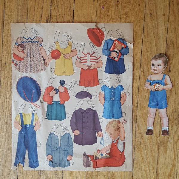 1930s toddler boy paper doll named Jimmy comes with lots of clothes and toys, including play clothes, a dress-up shorts outfit, and a book
