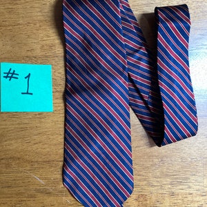 Puede incluir: Una corbata azul oscuro con finas rayas rojas y doradas. La corbata est&aacute; doblada por la mitad y colocada sobre una superficie de madera.