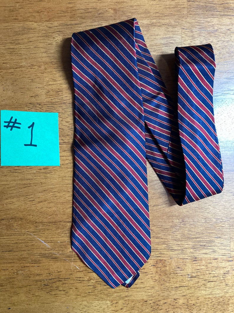 Puede incluir: Una corbata azul oscuro con finas rayas rojas y doradas. La corbata est&aacute; doblada por la mitad y colocada sobre una superficie de madera.