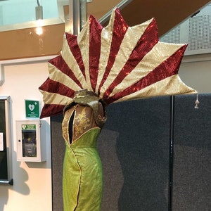 May include: A green sequined gown with a red lining and a large, red and gold fan-shaped headpiece.