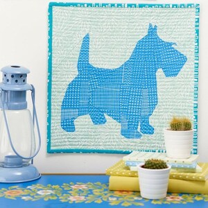 May include: A blue and white quilted wall hanging featuring a geometric design of a dog. The dog is outlined in white and has a blue patterned body. The background is a light green with a white floral pattern.