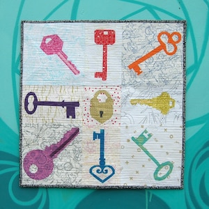 May include: A colorful quilt with a patchwork design featuring nine squares. Each square has a different key or lock design in various colors, including pink, purple, orange, yellow, and blue. The quilt is framed with a gray border.