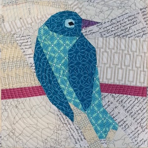 May include: A blue and teal bird with a white floral pattern is made from fabric scraps and sewn together. The bird is perched on a pink and white striped fabric. The background is a white fabric with a printed pattern.