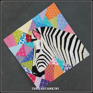 May include: A fabric art piece featuring a zebra head with black and white stripes. The zebra is set against a patchwork background of colorful triangles in various patterns and colors, including pink, blue, and orange. The text "THE TARTANKIWI" is at the bottom.