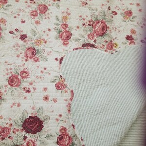 May include: A white quilted throw blanket with a floral pattern featuring red and pink roses. The reverse side of the blanket is a light green with white stripes.