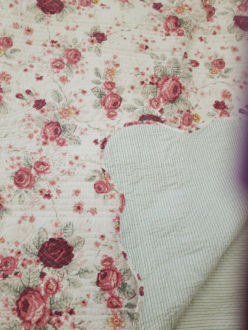 May include: A white quilted throw blanket with a floral pattern featuring red and pink roses. The reverse side of the blanket is a light green with white stripes.