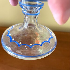 May include: Clear glass goblet with blue trim and a scalloped design. The base features a blue border with white dots. The stem is clear with blue accents. The rim has a blue border.