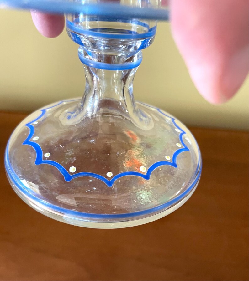May include: Clear glass goblet with blue trim and a scalloped design. The base features a blue border with white dots. The stem is clear with blue accents. The rim has a blue border.