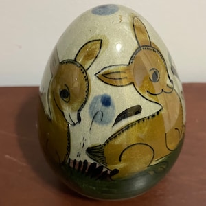 May include: A ceramic egg-shaped ornament with a hand-painted design of two brown deer with blue and green accents.