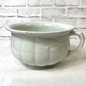 May include: White ceramic chamber pot with a single handle. The pot has a rounded body with a fluted design.