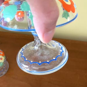 May include: Clear glass dessert dishes with a blue and white scalloped rim and floral design. The dishes have a stem and a rounded bowl, with orange, red, and green floral patterns. The rim has a blue border with white dots.