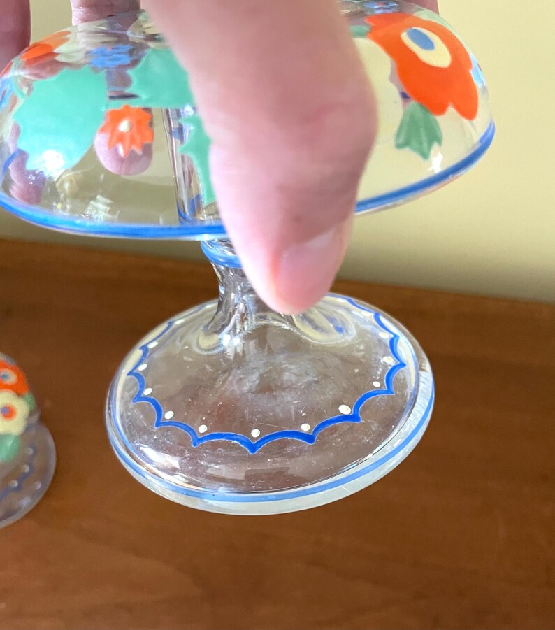 May include: Clear glass dessert dishes with a blue and white scalloped rim and floral design. The dishes have a stem and a rounded bowl, with orange, red, and green floral patterns. The rim has a blue border with white dots.