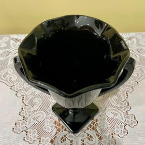 Peut inclure: Un vase en verre noir dot&eacute; d'un large bord festonn&eacute; et ondul&eacute; ainsi que de deux anses lat&eacute;rales. Le vase pr&eacute;sente une finition lisse et brillante et repose sur une base carr&eacute;e, vu d'un angle &eacute;lev&eacute; pour montrer l'int&eacute;rieur profond et sombre.