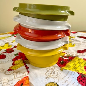 May include: A stack of five round plastic storage bowls with lids, featuring a vibrant color palette of olive green, white, orange, white, and yellow. Each bowl has two small side handles and a smooth, glossy finish, arranged vertically.