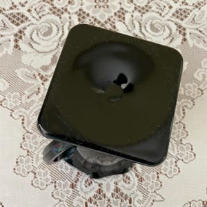Peut inclure: Un objet en verre noir avec un dessus carr&eacute; et une indentation circulaire au centre. L'objet pr&eacute;sente une surface lisse et r&eacute;fl&eacute;chissante avec une finition opaque sombre. La base est partiellement visible, montrant une structure en verre sombre.