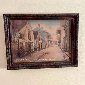 May include: A framed print depicting a street scene in Saint Augustine, Florida. The image shows historic buildings along Charlotte Street with a lamp post on the left. The text "Charlotte Street, Saint Augustine Florida" and "Harris" are visible.