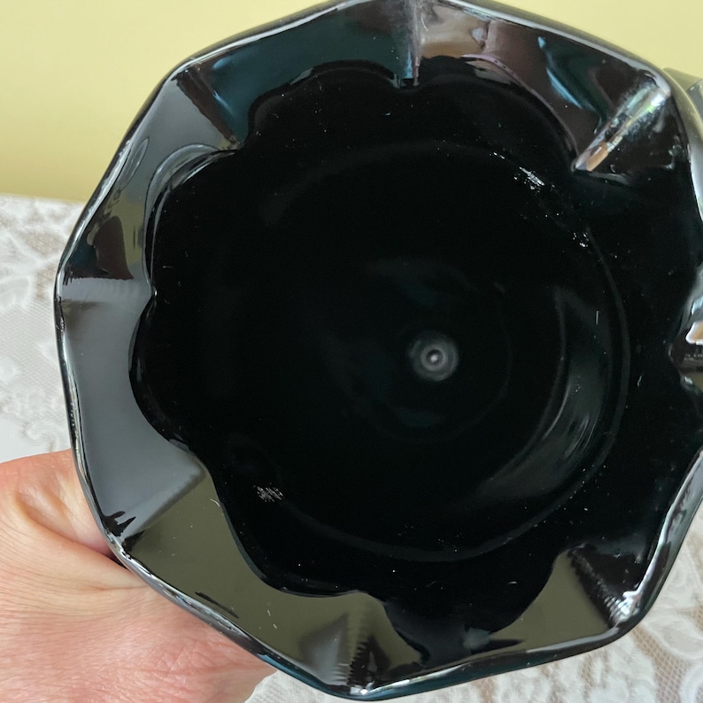 Peut inclure: Un vase en verre noir brillant dot&eacute; d'un large bord festonn&eacute; en forme de fleur. L'int&eacute;rieur du r&eacute;cipient est profond et sombre, pr&eacute;sentant une surface lisse et r&eacute;fl&eacute;chissante qui se r&eacute;tr&eacute;cit vers la base, cr&eacute;ant une silhouette &eacute;l&eacute;gante.