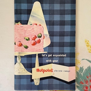 May include: A vintage Hotpoint electric range advertisement featuring a pink cake with red and green berries on a silver cake stand. The ad has a blue and white checkered background and the text "Let's get acquainted with your Hotpoint electric range".