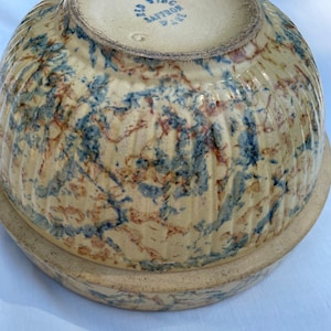 May include: Antique stoneware mixing bowl with a cream-colored base and a marbled pattern of blue and brown. The bowl has vertical ribbed detailing and a circular base. The bottom of the bowl is stamped with "RED WING SAFFRON WARE".